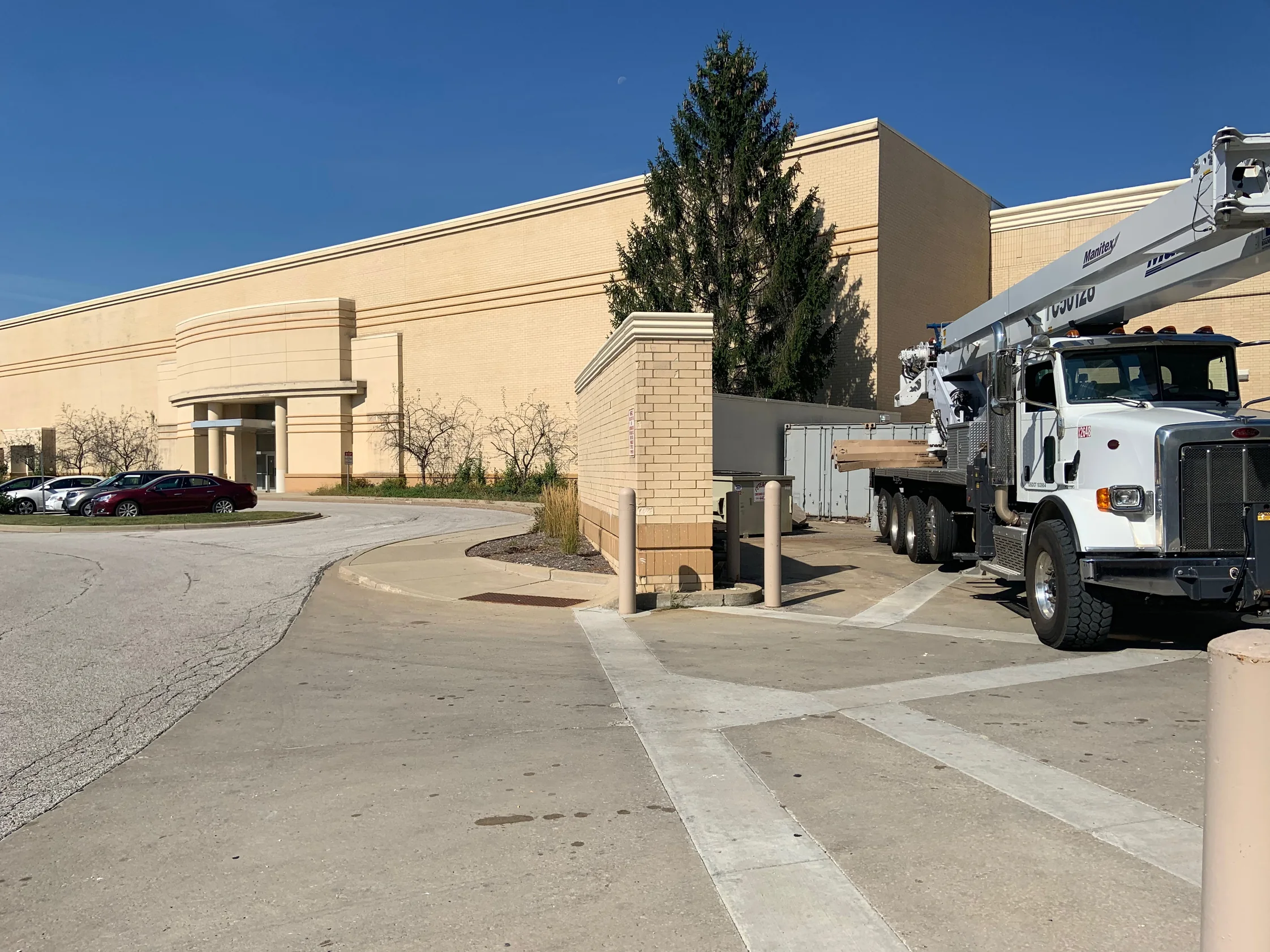 The long buff brick flank of the mall in 2019, running from a curved entrance canopy past a car park to a service yard