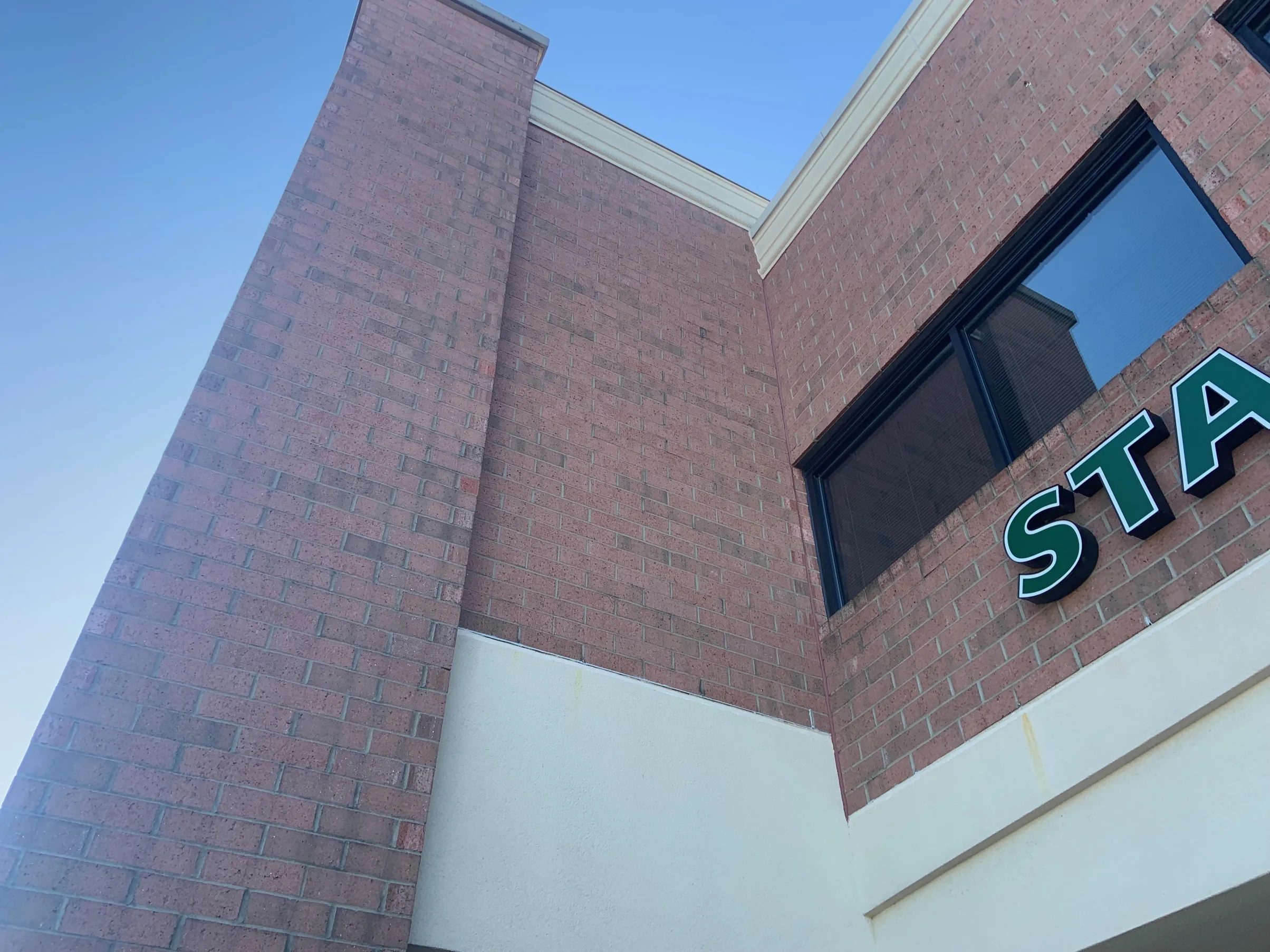 Two brick wall planes of the store meeting at a corner in 2019, seen from below against the sky, the brick even across both faces