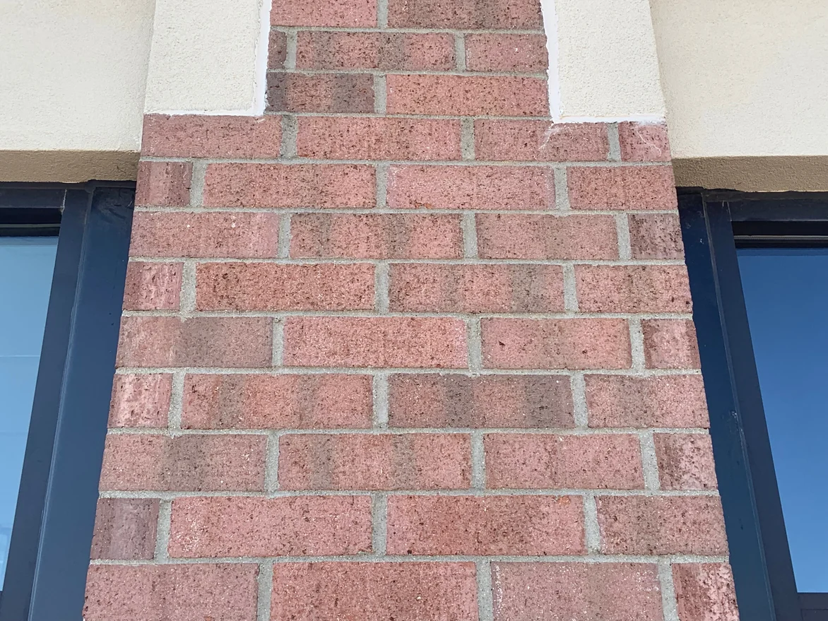 A brick pier between two windows in 2019, its units a mixed pink and red range with pale mortar joints