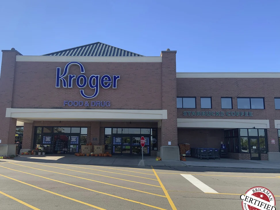 The front of the Kroger in 2019, its brick reading as one pink and red range across the store front and the coffee shop beside it.