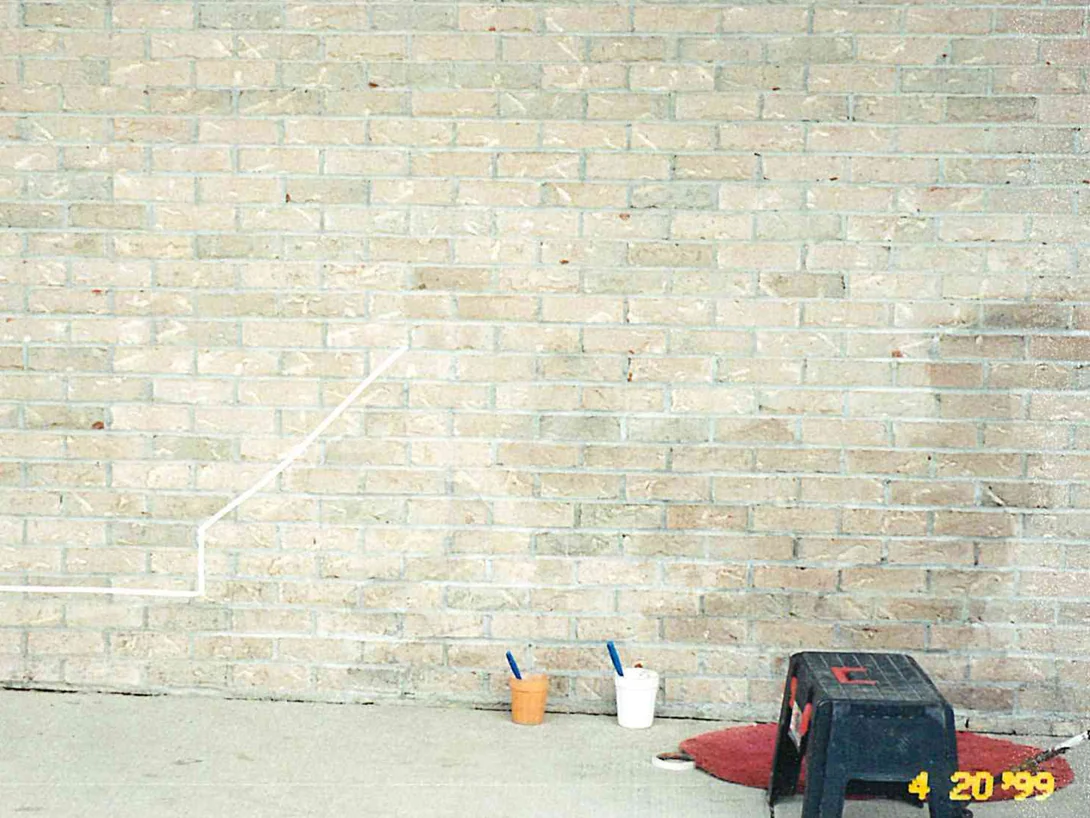The same buff brick wall part way through the work in 1999, a masking line stepped across the lower courses and two buckets of brushes standing on the sidewalk