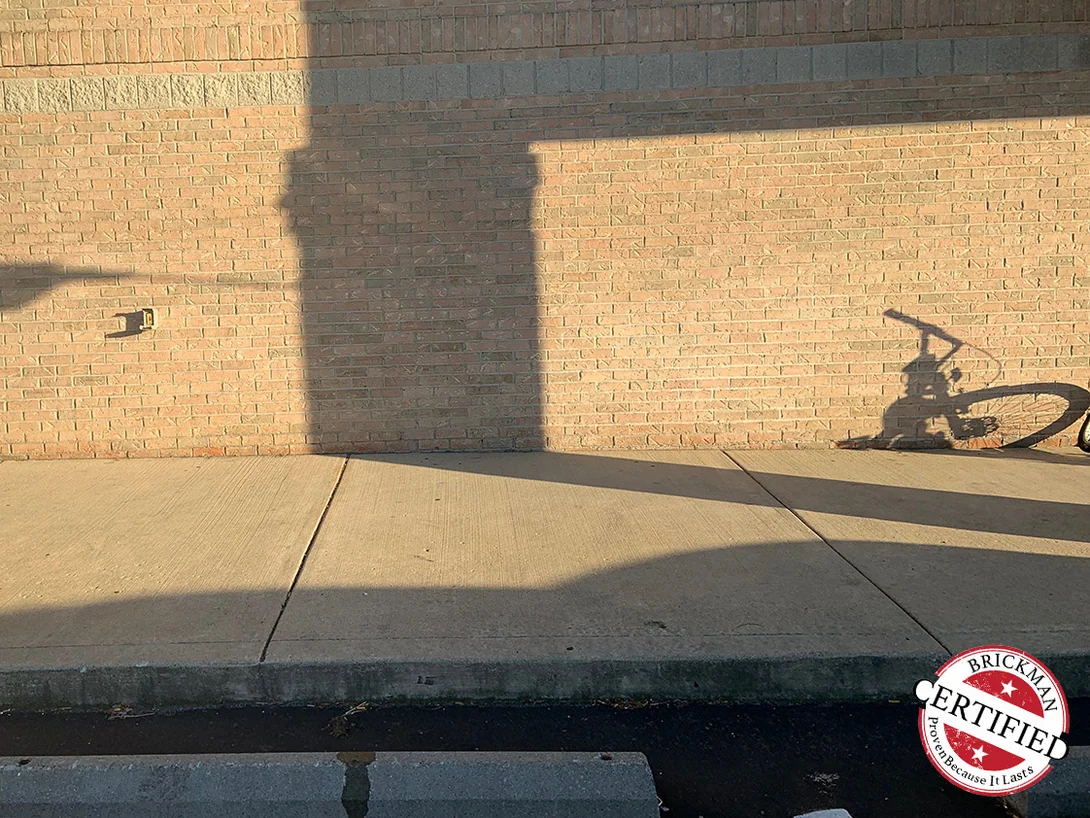 A stretch of the tan brick elevation above the sidewalk in low evening sun in 2019, an accent band of grey units running through the wall