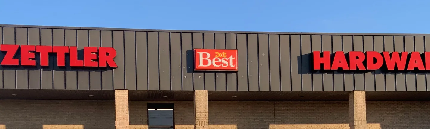 A single story hardware store in 2019, its tan brick piers and field wall under a dark metal fascia