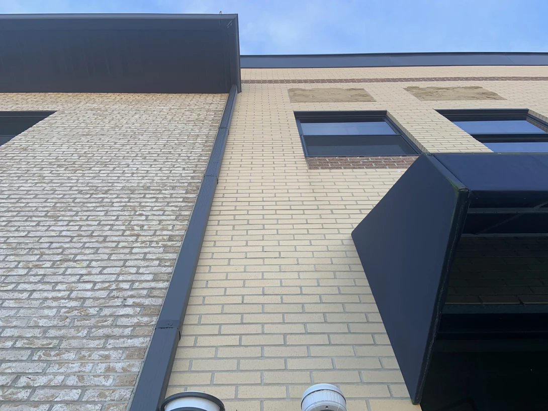 An inside corner in 2019 where a rough tan brick wall meets the smooth cream brick of the main elevation at a downspout