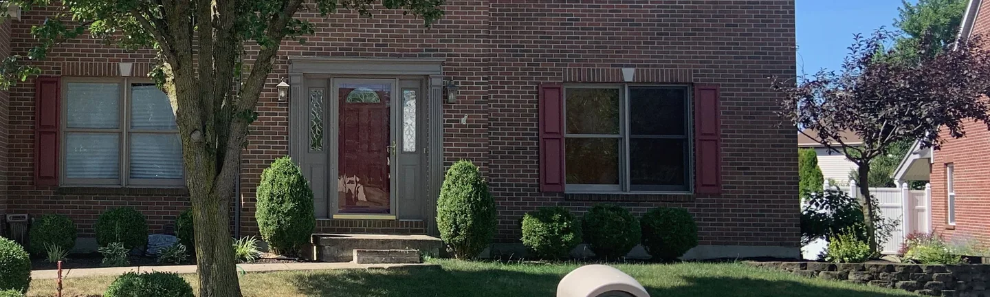 The brick around the front entry of the house in 2019, an even range of red and brown units running past the door and the shuttered windows