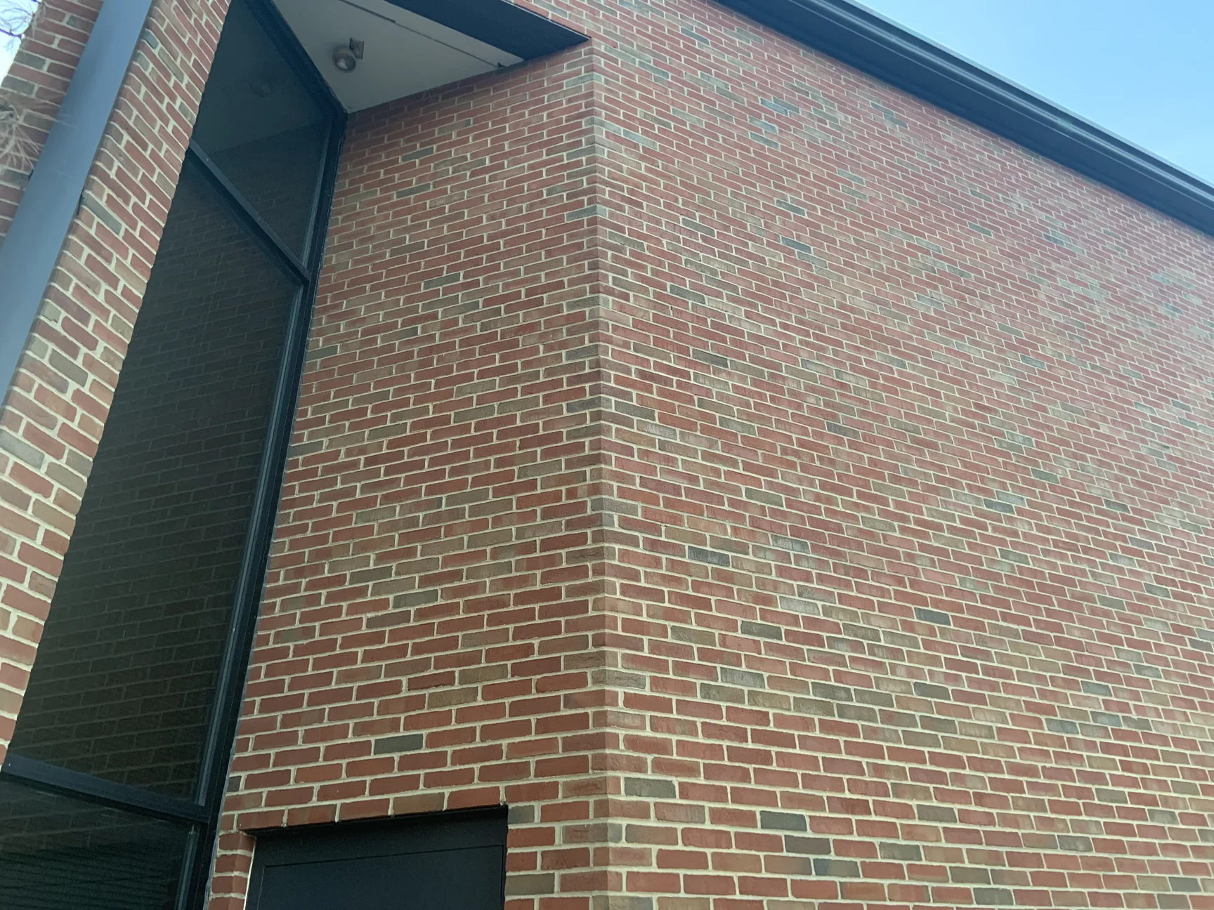 An outside corner of the building in 2019, red brick with scattered darker units running evenly around the corner and past a tall glazed bay