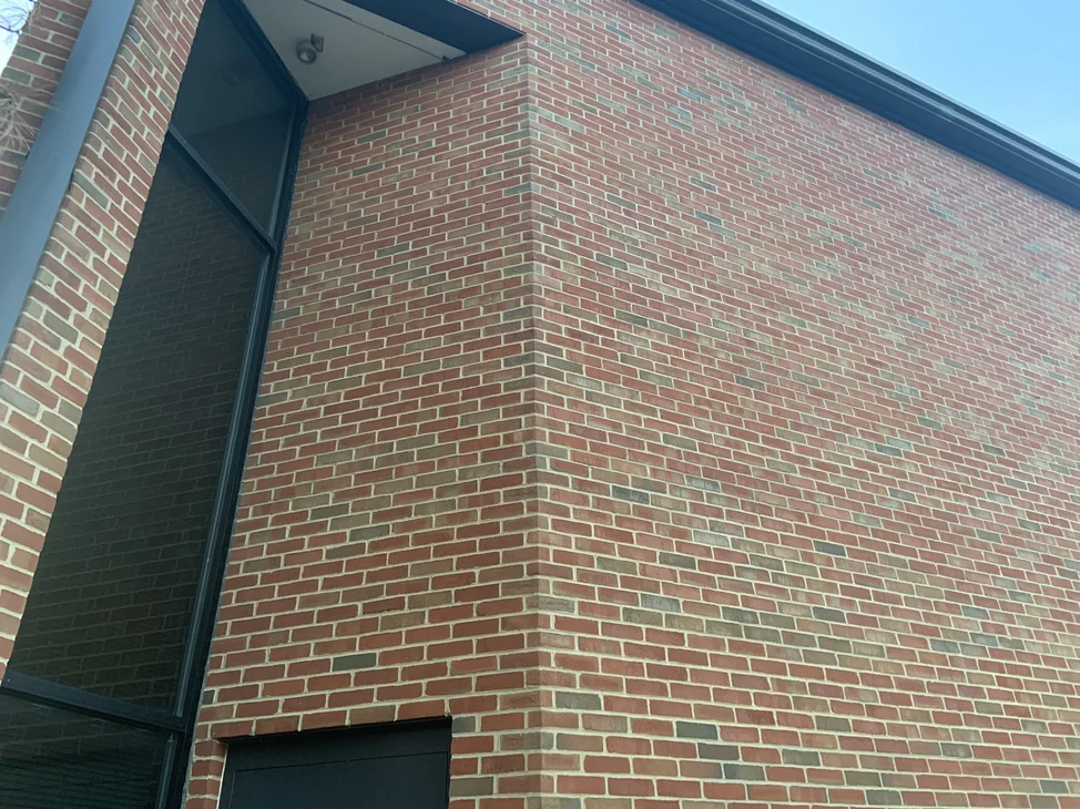 An outside corner of the Ohio university building in 2019, red brick with scattered darker units running evenly around the corner past a tall glazed bay