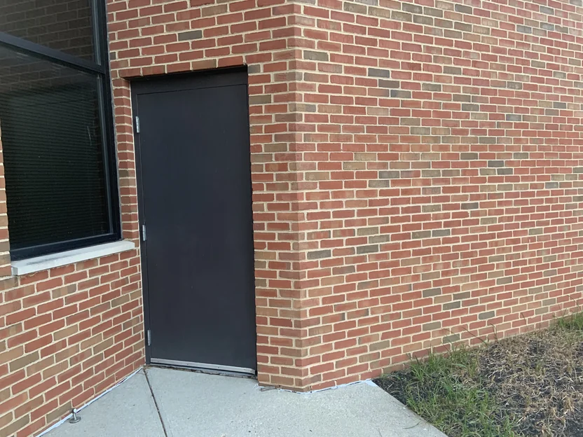 A service door set into the brick beside an outside corner in 2019, the corner units matching the field brick on both faces down to the sidewalk