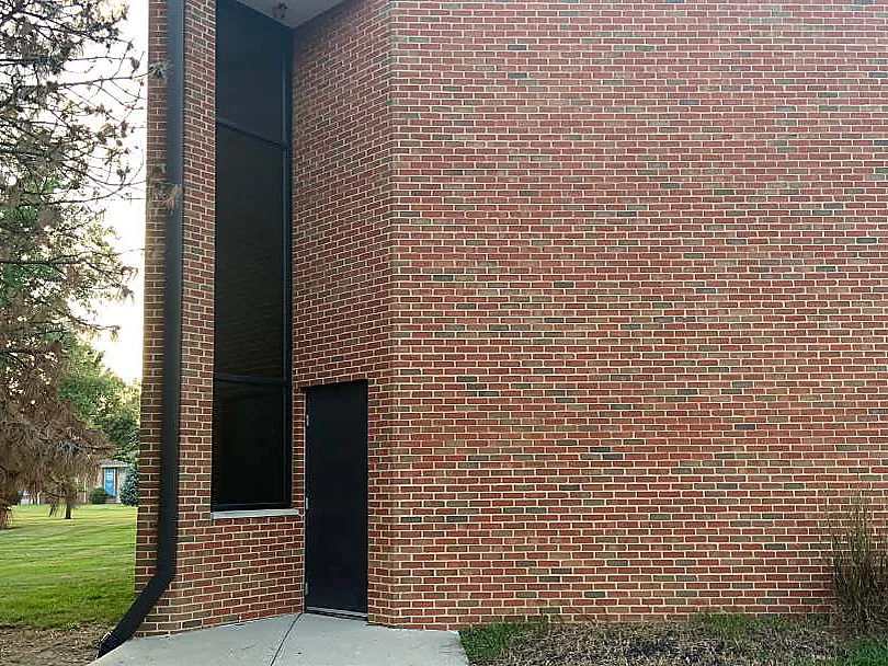The same end wall in 2019 with lawn and an evergreen where the dirt was, the patchy units gone and the brick reading as one range to the roofline