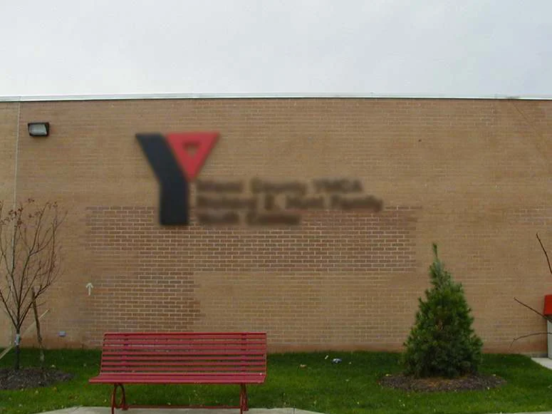 The front wall in 2002, a wide rectangle of redder fill-in brick standing out from the buff brick around it under the building sign, with a red bench on the walk below
