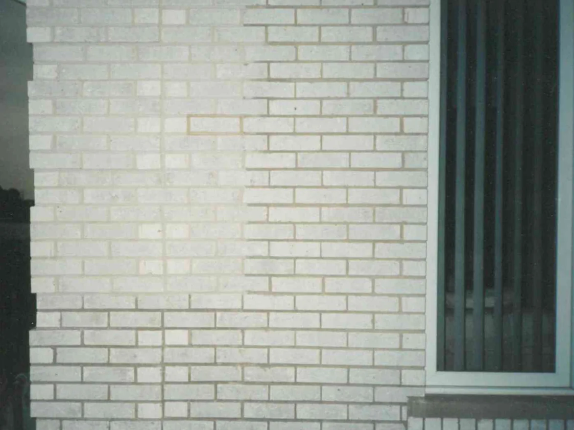 A wall of pale brick beside a window in 1998, a film print in which the mortar joints read a tan shade darker than the units around them, with one joint near the middle standing out lighter