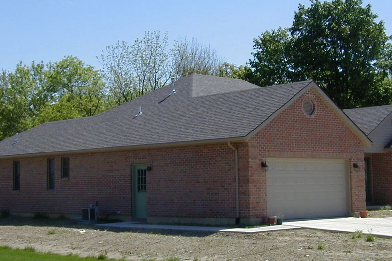 The long side of the house in 2002 with the garage bay beyond, its red brick carrying darker units in patches, the ground still bare from construction