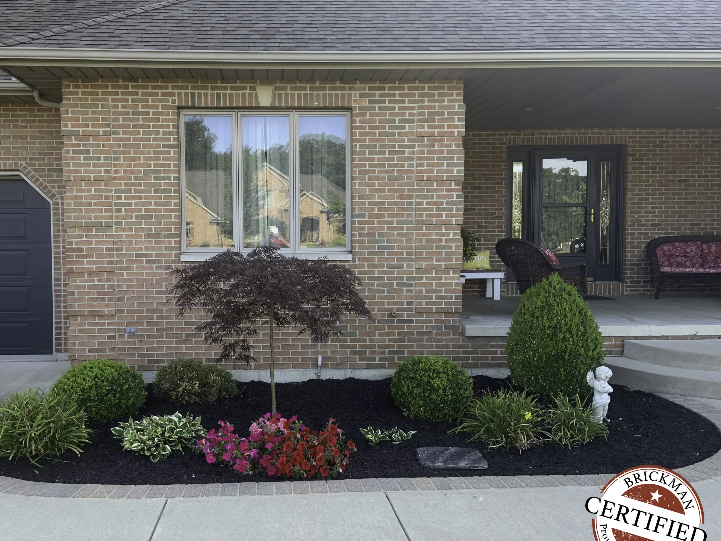 The front of the house in 2019, its brick reading as one even range across the garage bay, the window wall and the covered porch