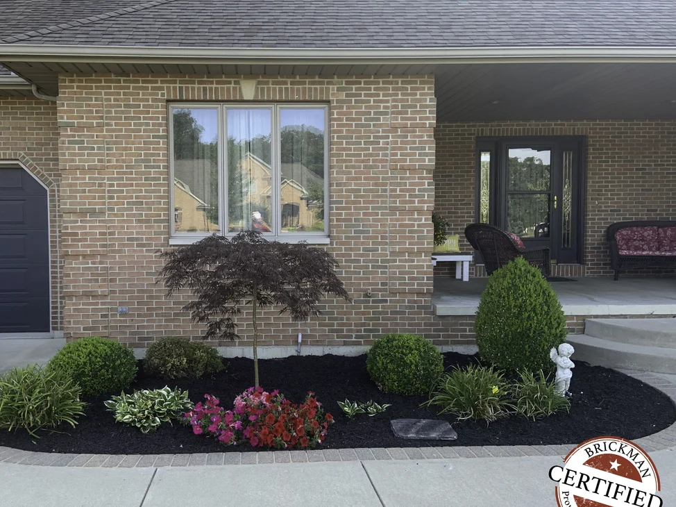 The front of the house in 2019, its brick reading as one even range across the garage bay, the window wall and the covered porch.