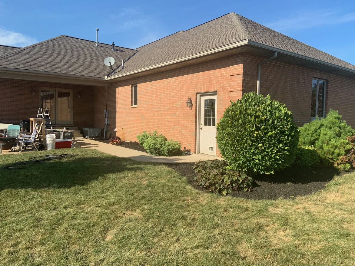 The rear corner of the house in 2019 with a service door and a covered patio beyond, the brick one consistent red from grade to eaves