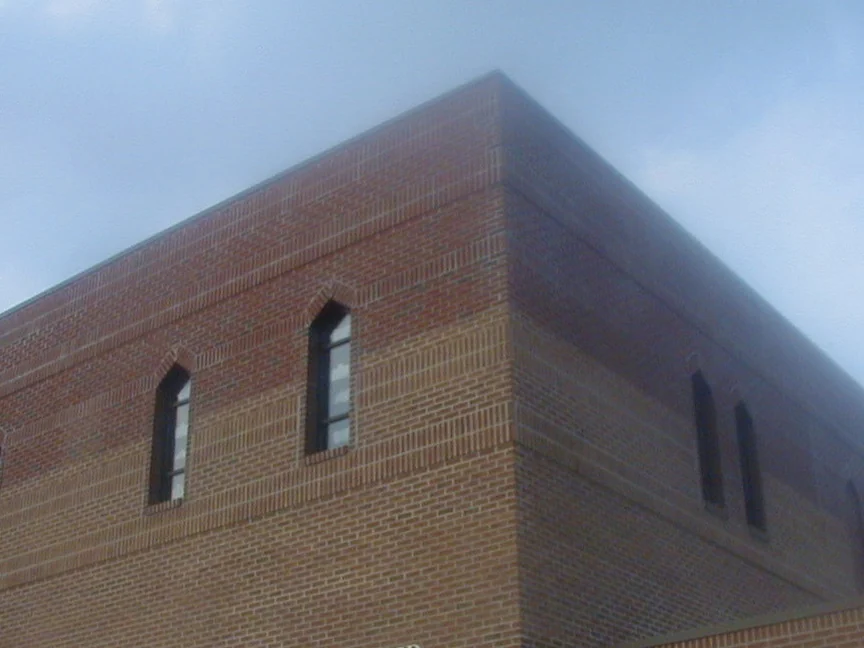 The upper corner of the church in 2004 before staining, the brick of the added second story reading lighter and flatter than the courses below the window line, pointed arch windows on both elevations