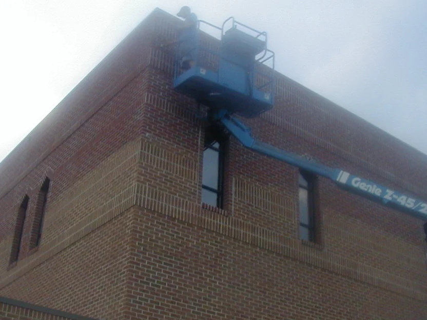 A blue articulating lift raised to the top corner of the second story in 2004, its basket against the parapet while the upper courses are stained