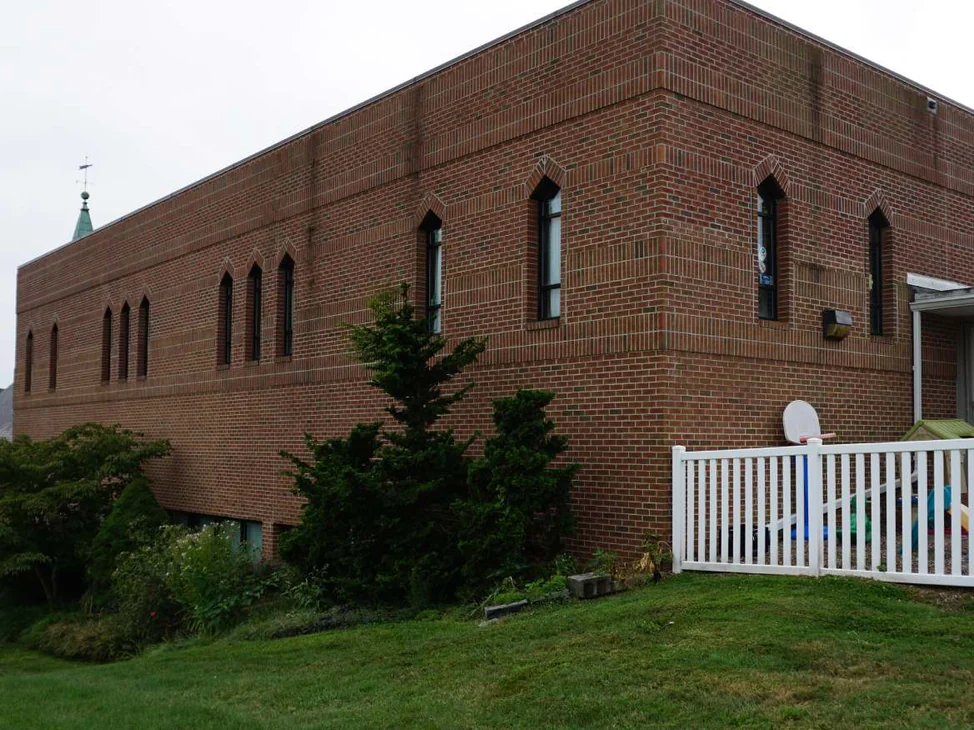 The long side of the church in 2019, two stories of red brick with pointed arch windows along the upper floor and a steeple behind