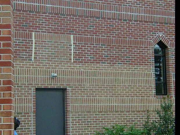 A rectangular test panel marked out on the second story brick beside a grey door in 2004, the area inside the outline reading a shade apart from the wall around it
