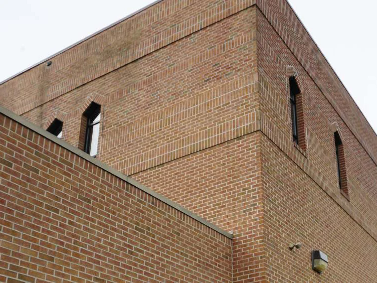 Looking up at the corner of the church in 2019, a lower wing in the foreground and the second story rising behind it, all one range of red brick