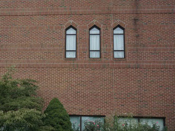The same three pointed arch windows in 2019, the brick above and below them one range, with a shrub against the ground floor windows