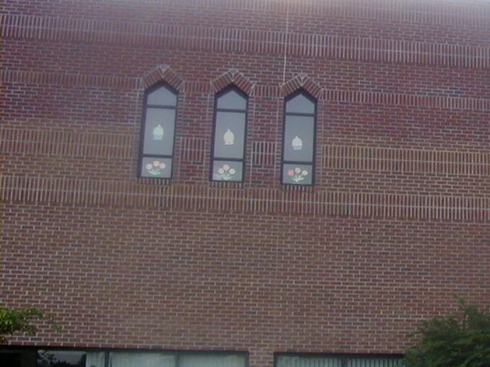Three pointed arch windows on the second story in 2004, the brick around them reading lighter than the original wall below, with sun glare at the top of the frame
