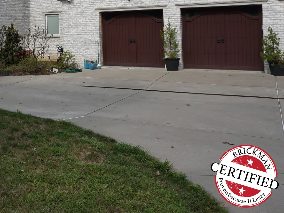 Two arched garage doors seen across the driveway in 2019, the surrounding brick an even pale grey, with the Brickman Certified stamp in the corner of the frame