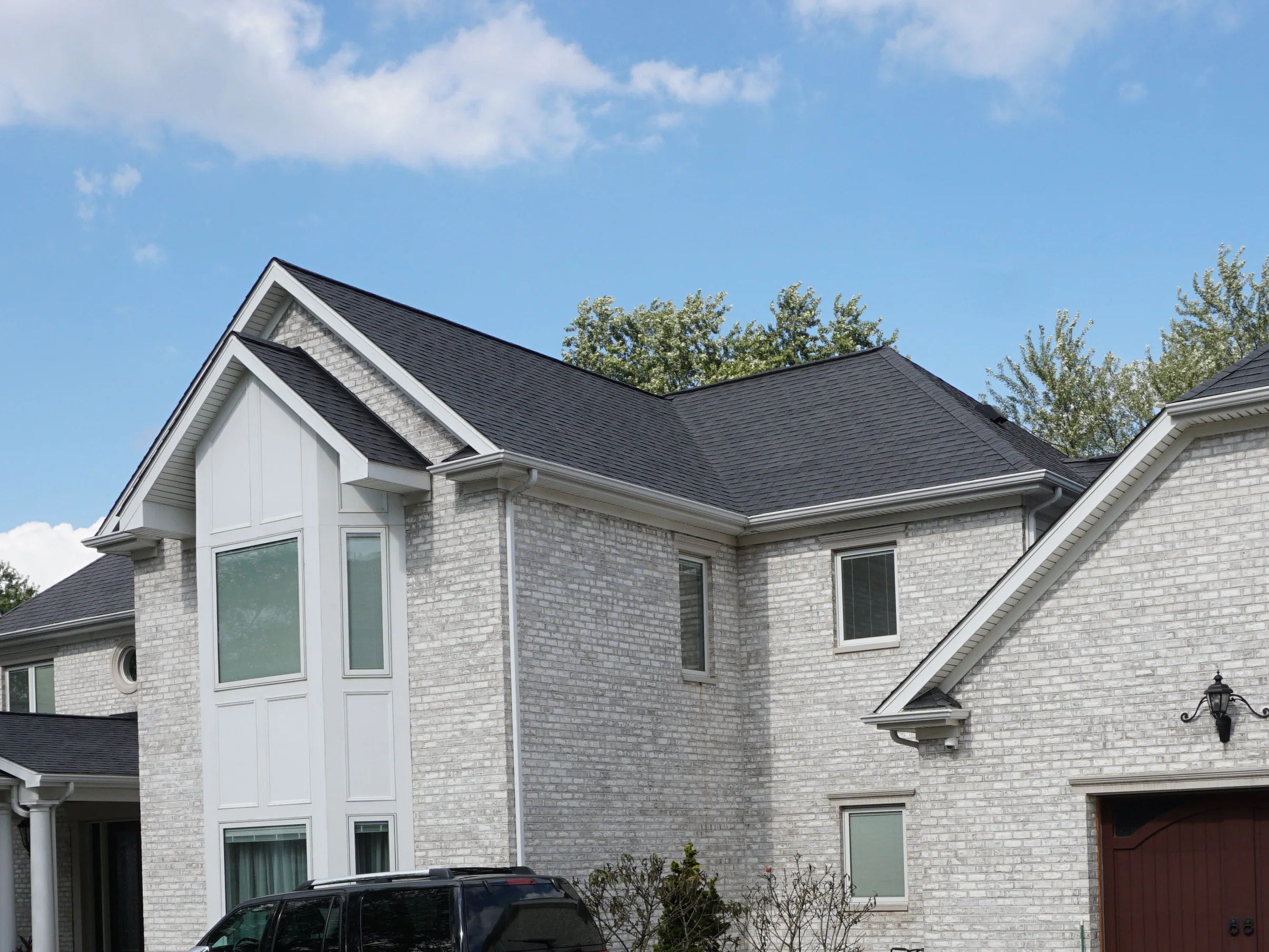The house from the driveway in 2019, its pale grey brick running unbroken across the main gable, the garage wing and the covered entry