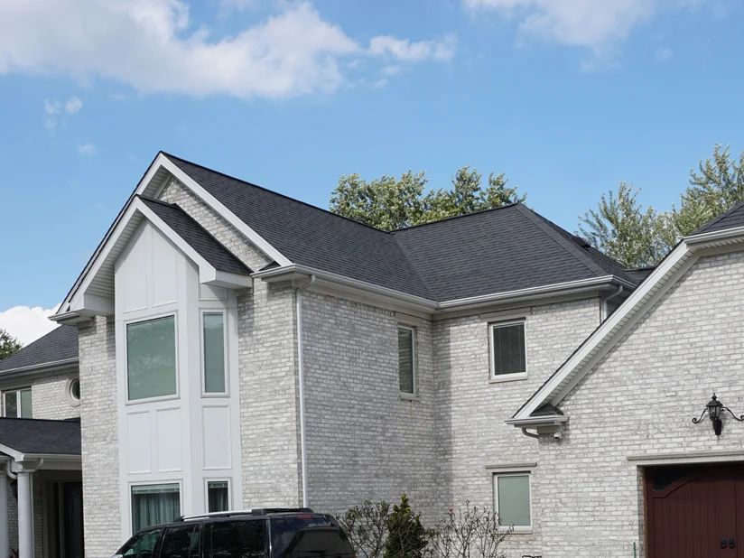 The house from the driveway in 2019, its pale grey brick running unbroken across the main gable, the garage wing and the covered entry.