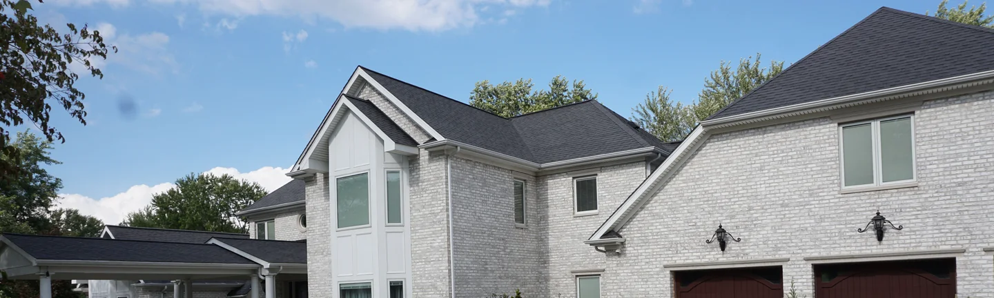 The house from the driveway in 2019, its pale grey brick running unbroken across the main gable, the garage wing and the covered entry