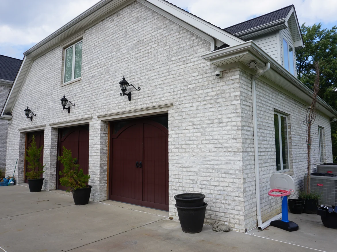The garage wing in 2019, three arched doors set in evenly coloured pale grey brick under a shingled gable