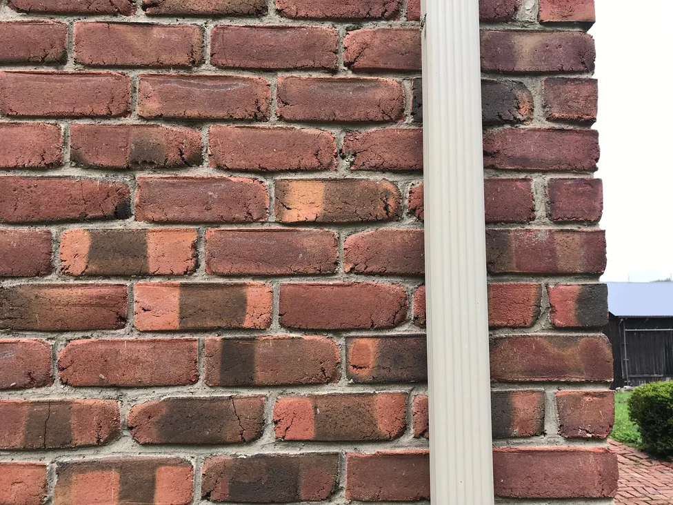 Close view of the brick at an outside corner in 2019, a downspout running down the angle and the units carrying the same range on both faces