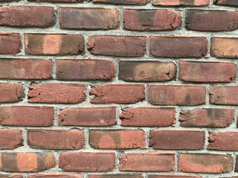 Close view of the brick face in 2019, individual units in mixed reds and deep browns with pale mortar joints between them