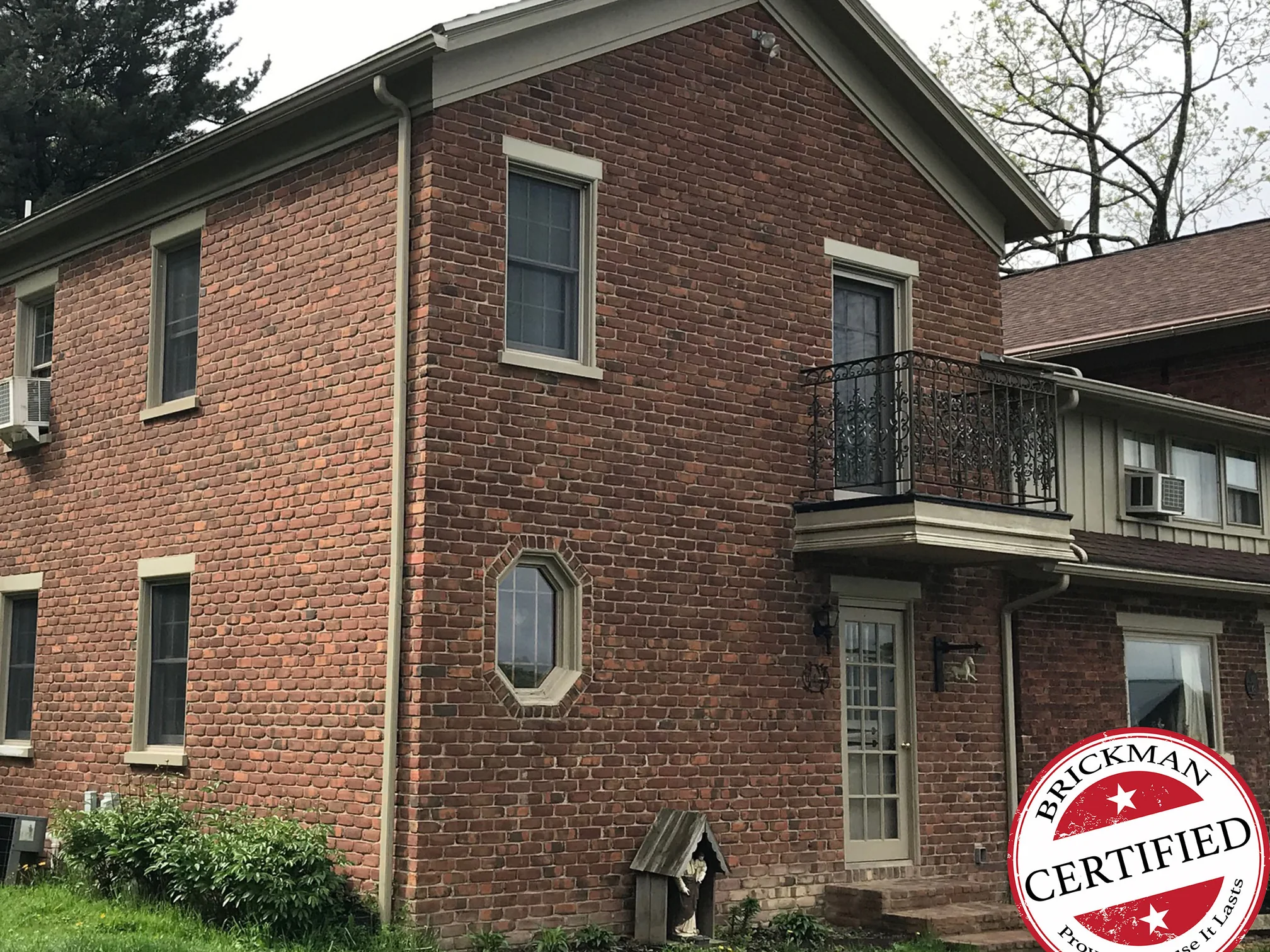 The same corner of the house in 2019, the brick reading as one range across the gable end and the long wall, with the Brickman certified stamp in the corner of the frame