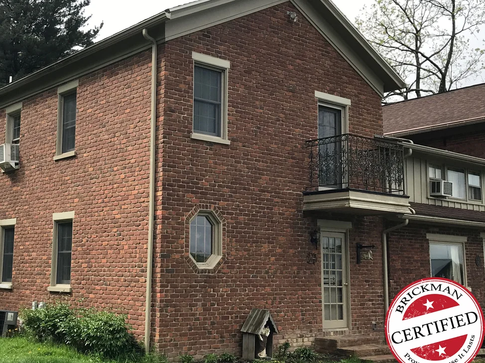 A two-story brick house in 2019, its brick reading as one even color across the gable and the long wall