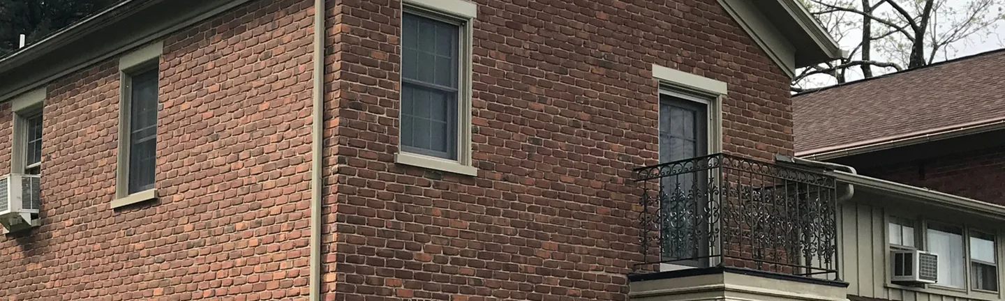 The brick of a two-story house in 2019, one even range across the corner below a wrought iron balcony