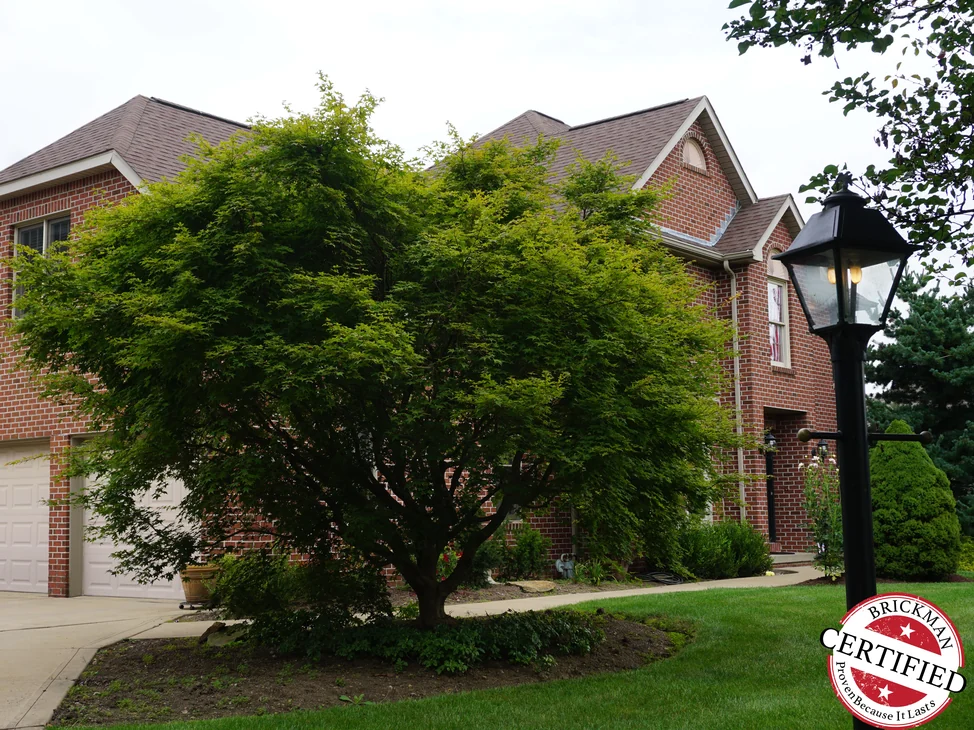 The house seen up its driveway in 2019, the garage wing and the main block reading as one red brick range behind a mature maple.