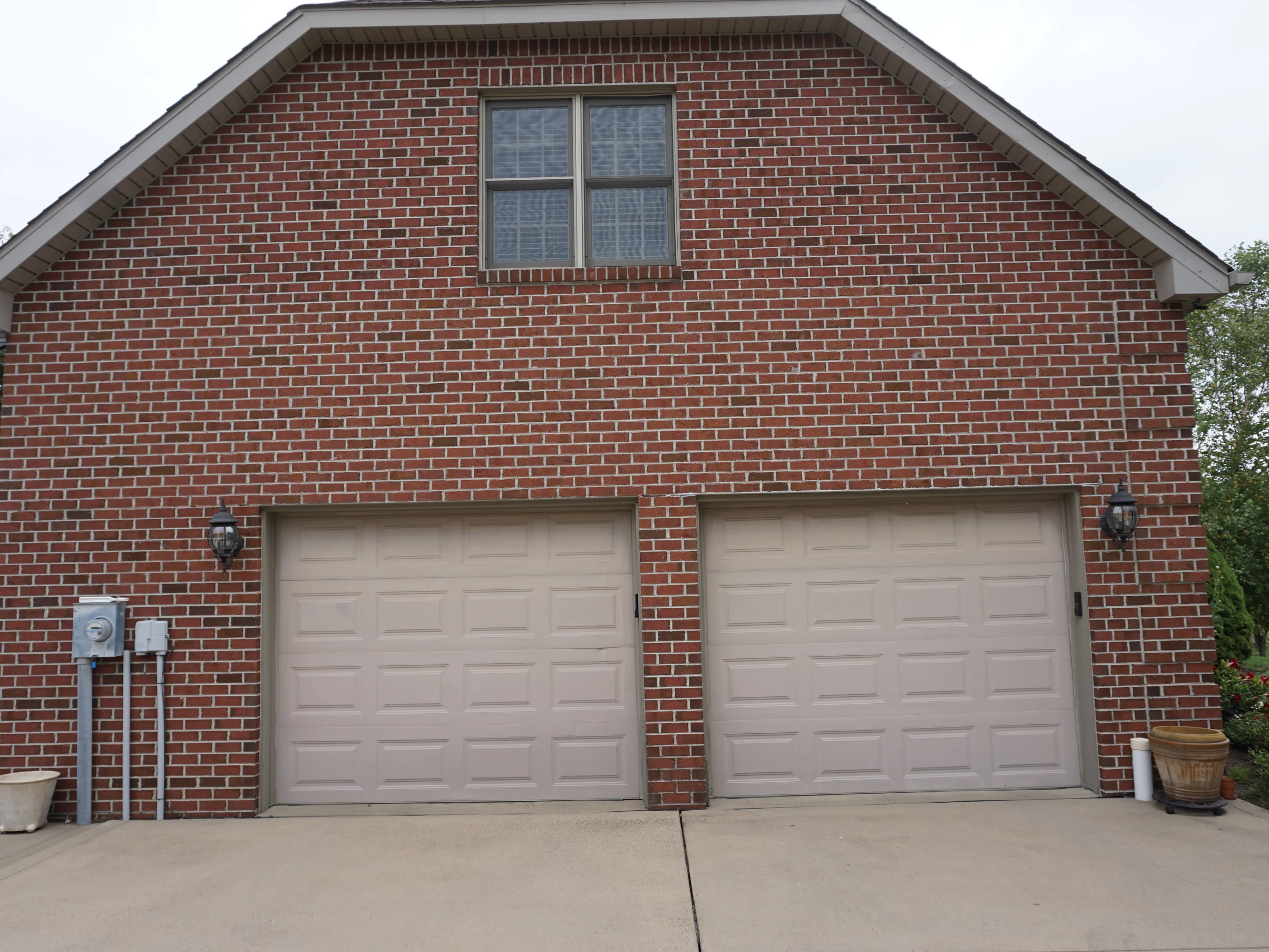 The garage gable end straight on in 2019, two doors under a full height wall of red brick with pale mortar joints