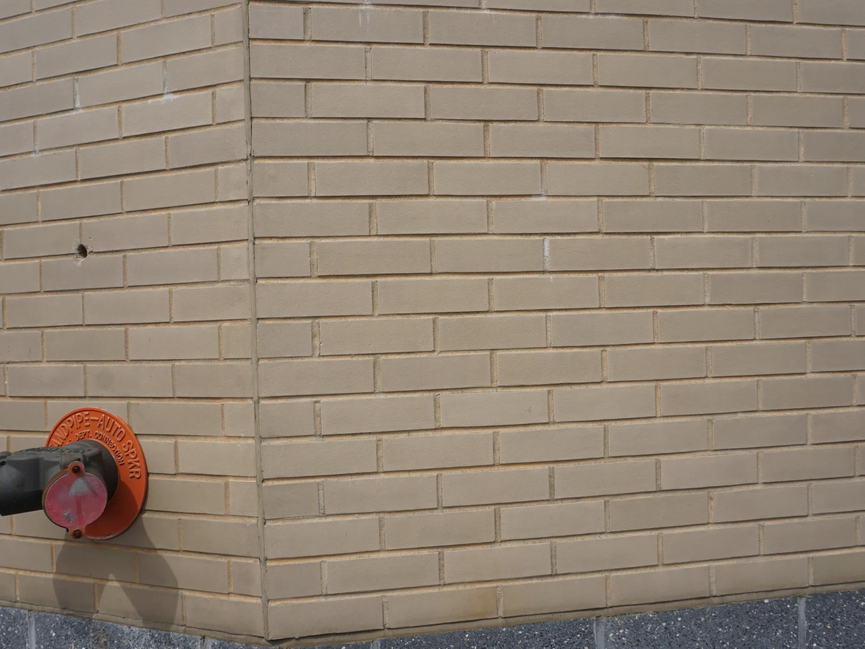 An outside corner of the hospital wall in 2019, the buff brick even in colour on both faces, with a fire department standpipe connection mounted at low level
