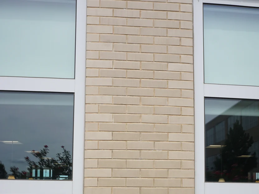A narrow brick pier between two windows in 2019, its buff brick matching the wall on either side