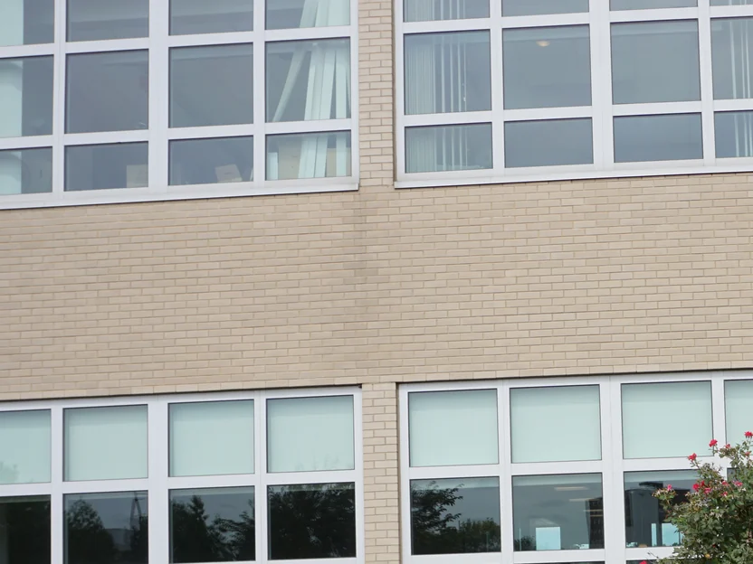 Two rows of windows in the hospital's buff brick wall in 2019, the brick between them one consistent colour