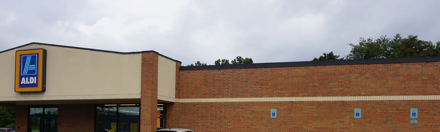 The front of the store in 2019, its lit ALDI sign over the entrance canopy and the brick wall running away along the parking lot
