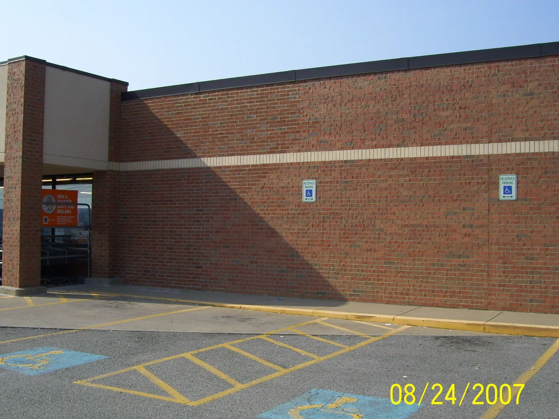 The store entrance in 2007, a red brick pier at the corner beside the doors and the long wall running back along the parking lot under a cream banding course