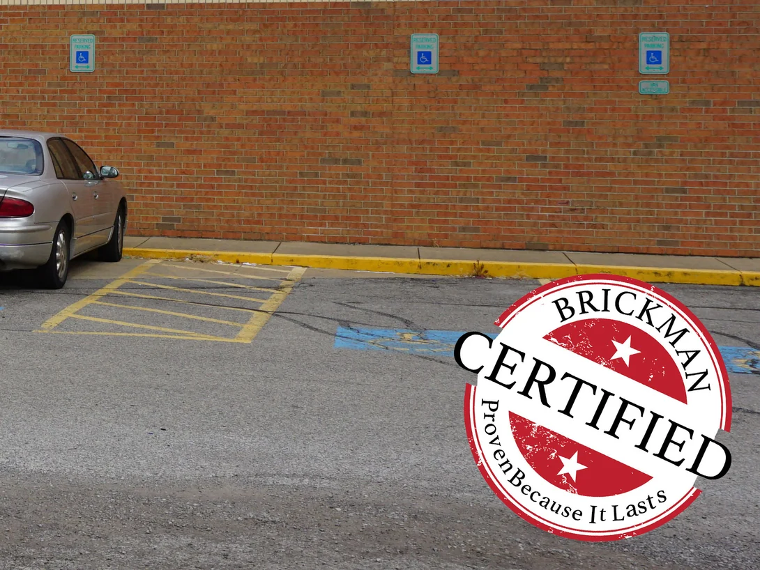 The wall along the reserved parking bays in 2019, its brick reading as a range of red, tan and grey brown from the roof edge down to the yellow kerb