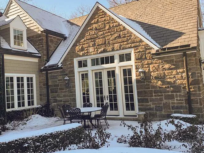 The gable and French doors in 2021, the addition's stone in the same range as the wing beside it, with a table and chairs on a snow covered terrace