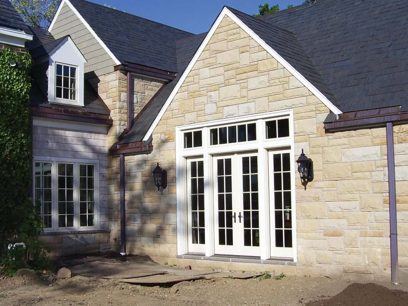 The new addition in 2006, a pale cream stone gable over a French door bay, standing on bare graded dirt beside the older wing