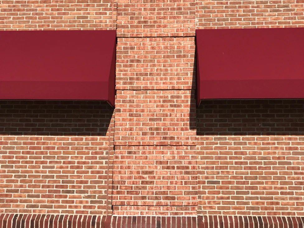 Close view of a brick pier meeting the wall on either side of it in 2019, the units reading in mixed reds and oranges against pale mortar