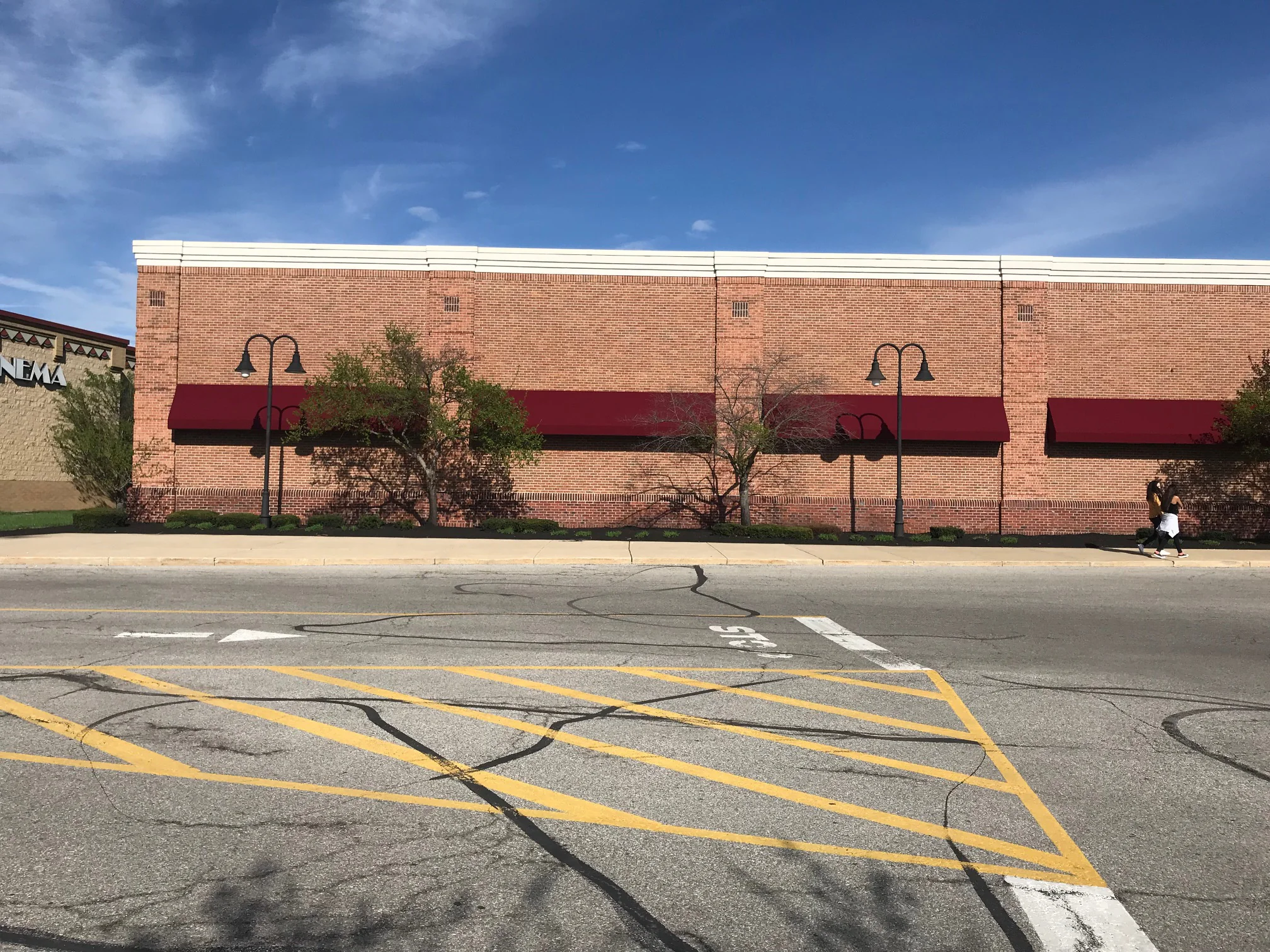 The long side wall of the store seen from across the access road in 2019, maroon awnings running its length and a cinema entrance at the far end
