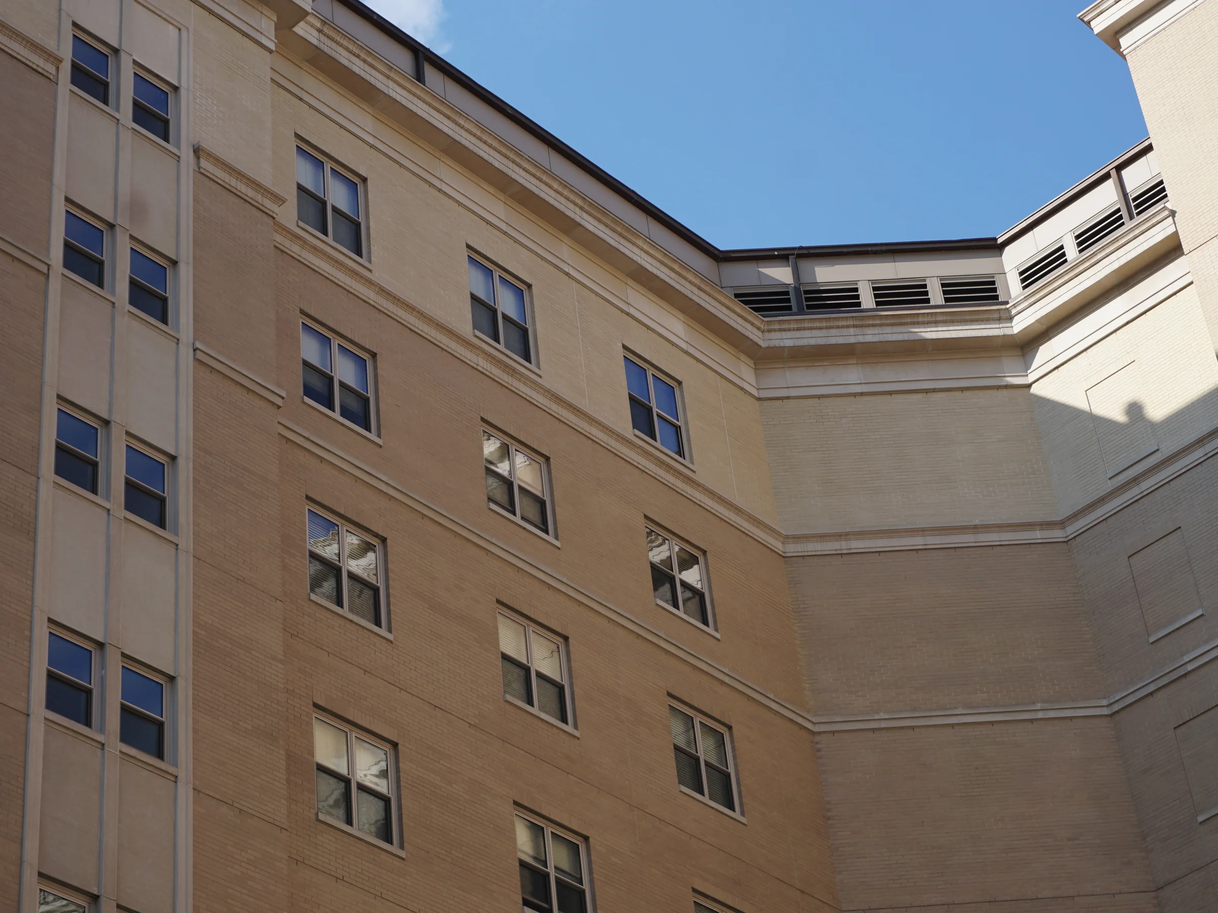 The inside corner of the college courtyard in 2019, one wing in warm tan brick and the wing beside it in pale buff, both running the full height of the frame