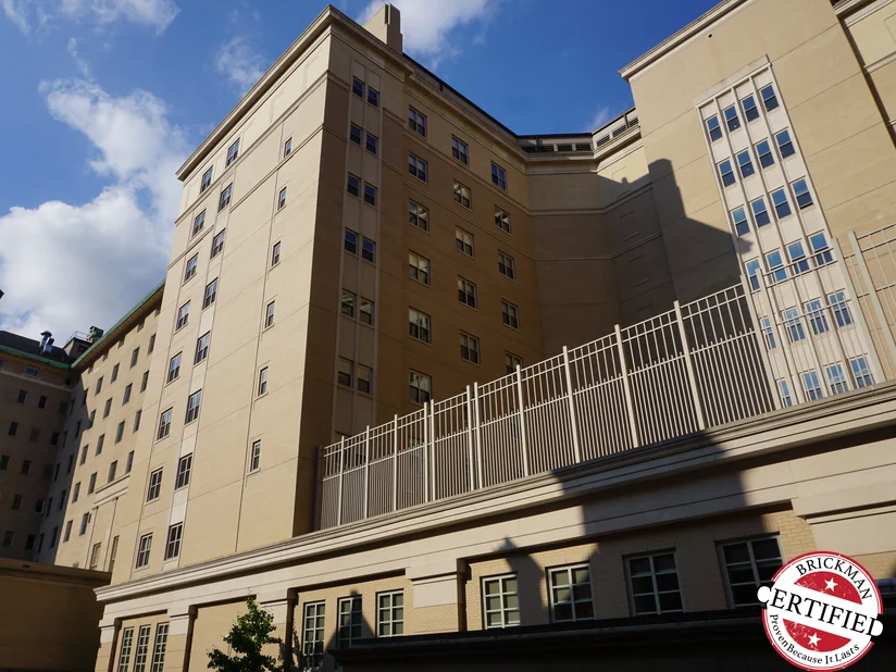 The college building from the courtyard in 2019, a tan brick tower rising above a lower brick wing behind an iron railing.